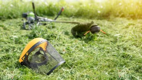 String trimmer and protective face mask on mown grass, sunlight, banner 16x9  Fotos Stock