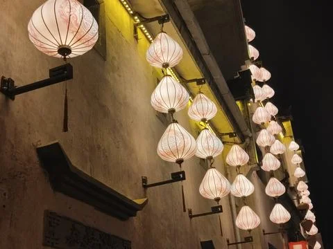 A string of white lanterns hangs on the wall, suspended from above at night.. Stock Photos