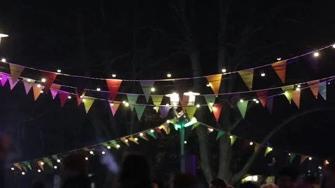 Strings of festive lights and flags hung in the park among the lanterns at night Stock Footage 240749919