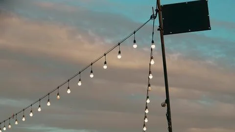 Strings of illuminated outdoor light bulbs hang diagonally from a pole agains Stockfoto's