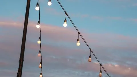 Strings of illuminated outdoor light bulbs hang diagonally from a pole agains Stockfoto's
