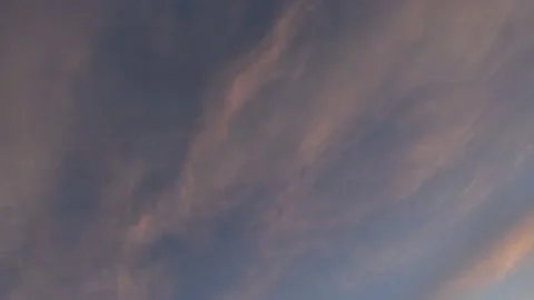 Stringy pink colored sunset clouds moving diagonally across a blue sky Stock Footage 151834696