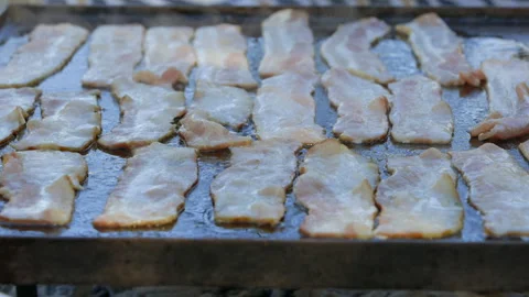 Stripe pattern as strips of bacon fry on large hot griddle outside Stock Footage 302189110