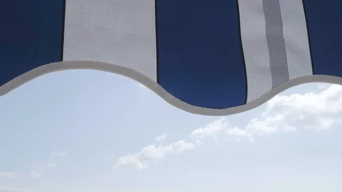 Striped awning gently moved by the wind against blue sky on sunny day Stock-Footage 129666948