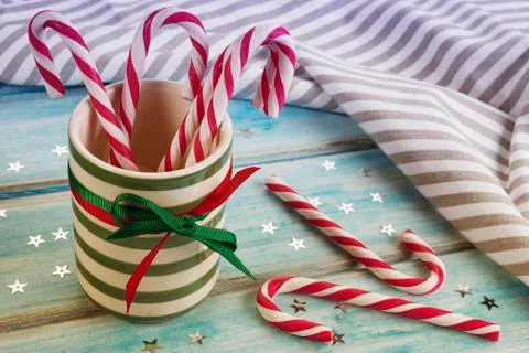 Striped ceramic cup with candy canes on a blue wooden table. Stock Photos
