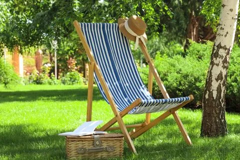 Striped deck chair with sun hat and picnic basket in garden Stock Photos