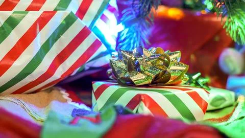 Striped Gift Box with Red Bow Under a Christmas Tree with Multicolored Lights Stock Photos
