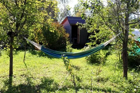 A striped hammock hangs between apple trees in a garden opposite a barn Foto stock