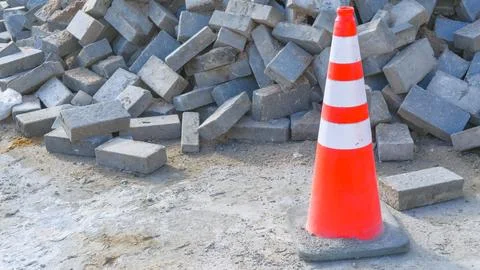 Striped orange traffic cone in front of concrete bricks or slabs, road repair Stock Photos