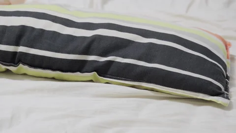 Striped pillow lying on white bed sheet Stock Footage 336125948