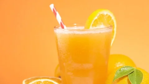 Striped straw falling into a Fresh Orange Juice on orange background Stock Footage 244623197