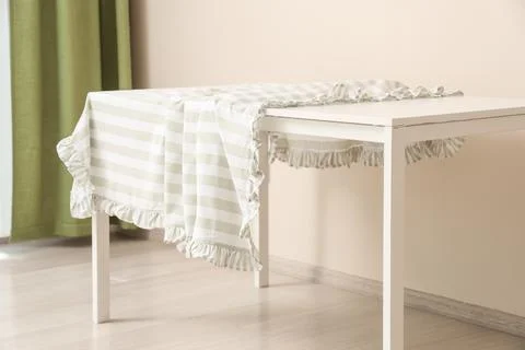 Striped tablecloth with ruffles draped over a white table in a room with gree 스톡 사진
