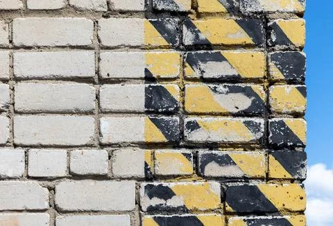 Striped yellow black Caution pattern is on the corner of gray brick wall Stockfoto's