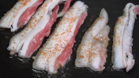 Strips of Streaky raw Bacon Slices Cooking in a Black Frying Pan. 스톡 동영상 334643017
