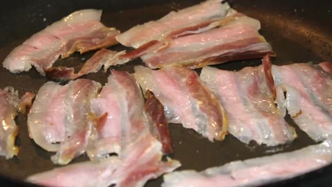 Strips of Streaky raw Bacon Slices Cooking in a Black Frying Pan. 스톡 동영상 334643227