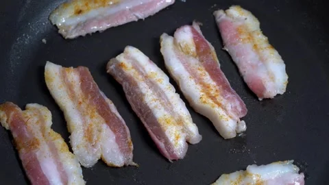Strips of Streaky raw Bacon Slices Cooking in a Black Frying Pan. 스톡 동영상 334643257