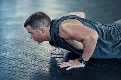 Strive for progress not perfection. a young man doing push ups in a gym. Stock Photos