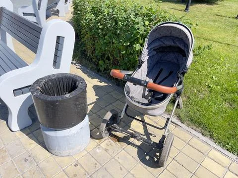 A stroller and a garbage can outside on a sunny day. Stock Photos