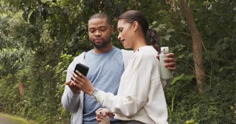 Strolling onto park path, Couple pulling smartphone and holding water bottle Stock Footage 338061073
