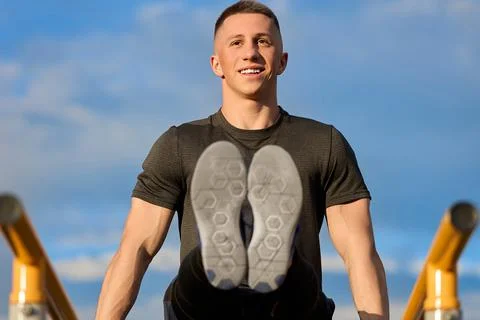 Strong athlete performs a complex exercise on parallel bars, trains outdoors Stock-Fotos