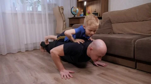 A strong athletic father doing push-ups with his son on his back at home. Stock Footage 305293431