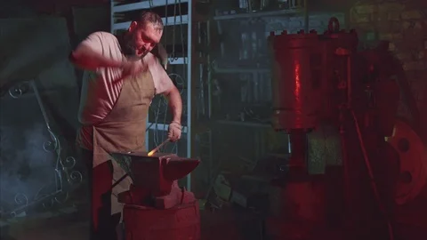Strong bearded blacksmith is hitting the hammer on a red hot rod Stock Footage 108032731