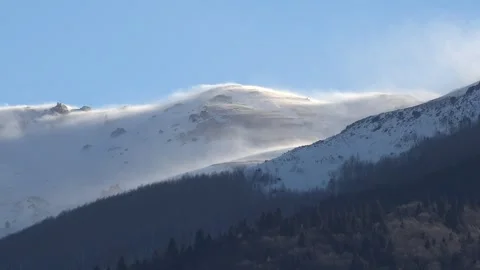 Strong blizzard wind sculpts snow surface across high mountain slope under clear Stock Footage 339374555