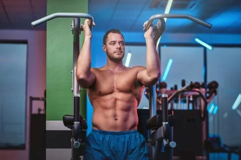 Strong bodybuilder doing excersise on a parallel bars in a modern fitness center Stock Photos