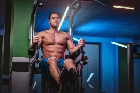Strong bodybuilder doing excersise on a parallel bars in a modern fitness center Stock Photos