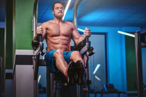 Strong bodybuilder doing excersise on a parallel bars in a modern fitness center Foto stock