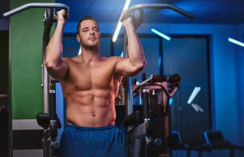 Strong bodybuilder doing excersise on a parallel bars in a modern fitness center Stock Photos
