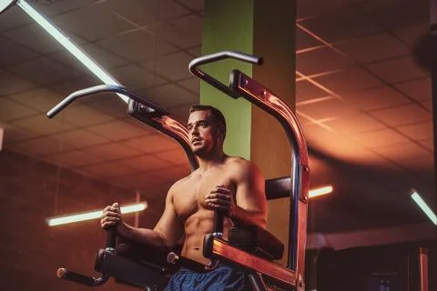 Strong bodybuilder doing excersise on a parallel bars in a modern fitness center 스톡 사진