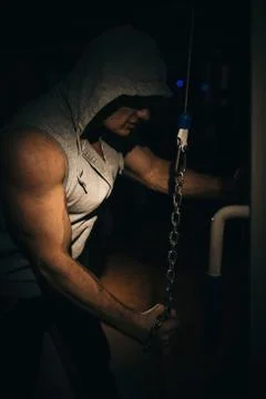 A strong bodybuilder makes triceps exercises with a chain in the gym. Stock Photos