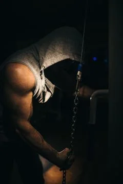 A strong bodybuilder makes triceps exercises with a chain in the gym. Stock Photos