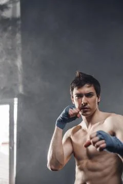 Strong boxer in the rays of the sun and smoke training hands with boxing wraps Stock-Fotos
