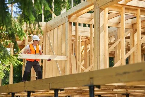 Strong builder constructing wooden house, building, wearing yellow vest and Stock Photos