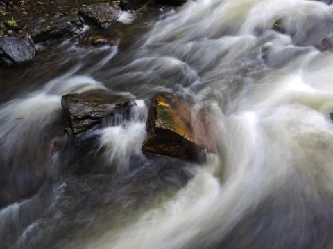 Strong current in river passing rocks with long exposure Stock Photos