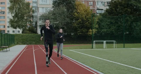 Strong disabled man overtake young woman while they run on race track. Male Stock Footage 148613333
