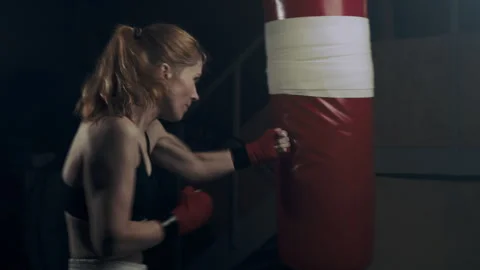 Strong female fighter practicing fast and strong hand strikes on a punching bag Stock Footage 273246748