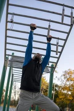 Strong Grey-Haired Man With Dreadlocks rearranges his hands on horizontal monkey Stock Photos