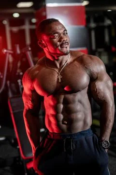 Strong halfnaked african american bodybuilder standing in contemporary gym an Stock Photos