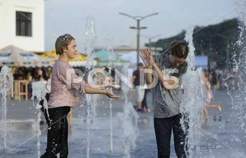 Strong heat in the city. Girls playing with fountain water jets on the square Stock Photos
