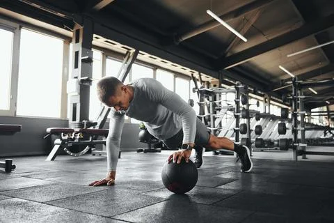 Strong male doing push up exercise with one hand on medicine ball during intense Stock Photos
