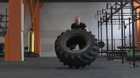Strong man doing big tire flips exercise in cross fit gym Stock Footage 88693065