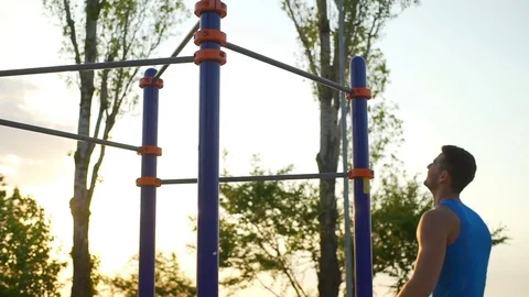 Strong man doing pull ups on horizontal bar park sunrise workout slow motion Stock Footage 76780356