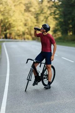 Strong man drinking water while standing on road with bike Foto stock