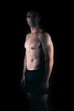 Strong man facing the camera while the light lighting his torso Stock Photos