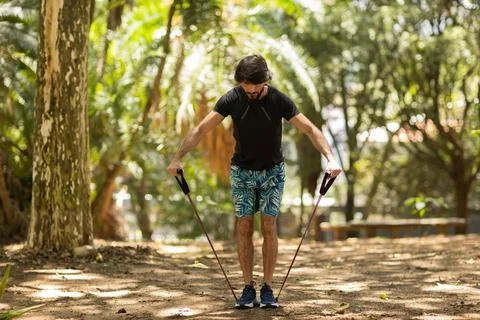 Strong man guy working out with elastic rubber bands at a park outdoors. Athl Stock Photos