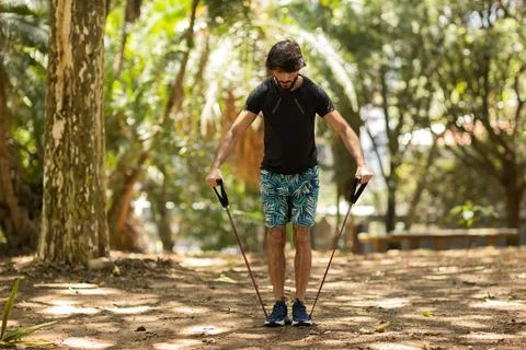 Strong man guy working out with elastic rubber bands at a park outdoors. Athl Stock Photos