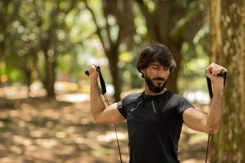 Strong man guy working out with elastic rubber bands at a park outdoors. Athl Stock Photos